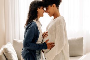 Duas mulheres sorrindo e segurando barriga da mulher grávida.