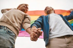 Dois homens de mãos dadas segurando bandeira lgbt