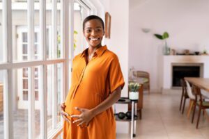 Mulher negra e madura grávida utilizando um vestido laranja.